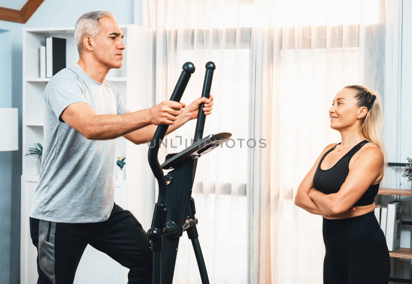 Active senior couple running on elliptical running machine at home together as fitness healthy lifestyle and body care after retirement for pensioner. Clout