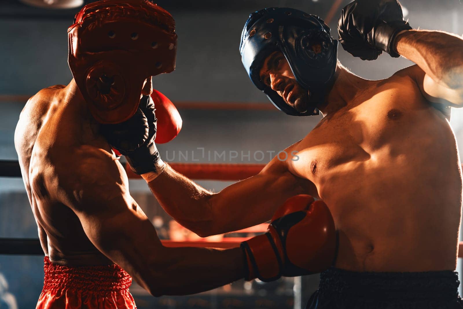 Two athletic and muscular body boxers with safety helmet or boxing head guard face off in fierce boxing match. Boxing fighter competitor fighting in the boxing ring. Impetus