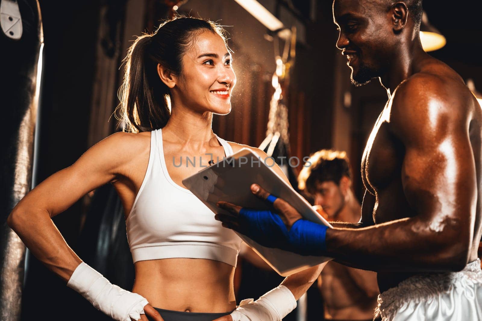 Asian female Muay Thai boxer and her personal boxing trainer discussing on her physical progress in the gym reflecting commitment to her body muscle growth and boxing performance. Impetus