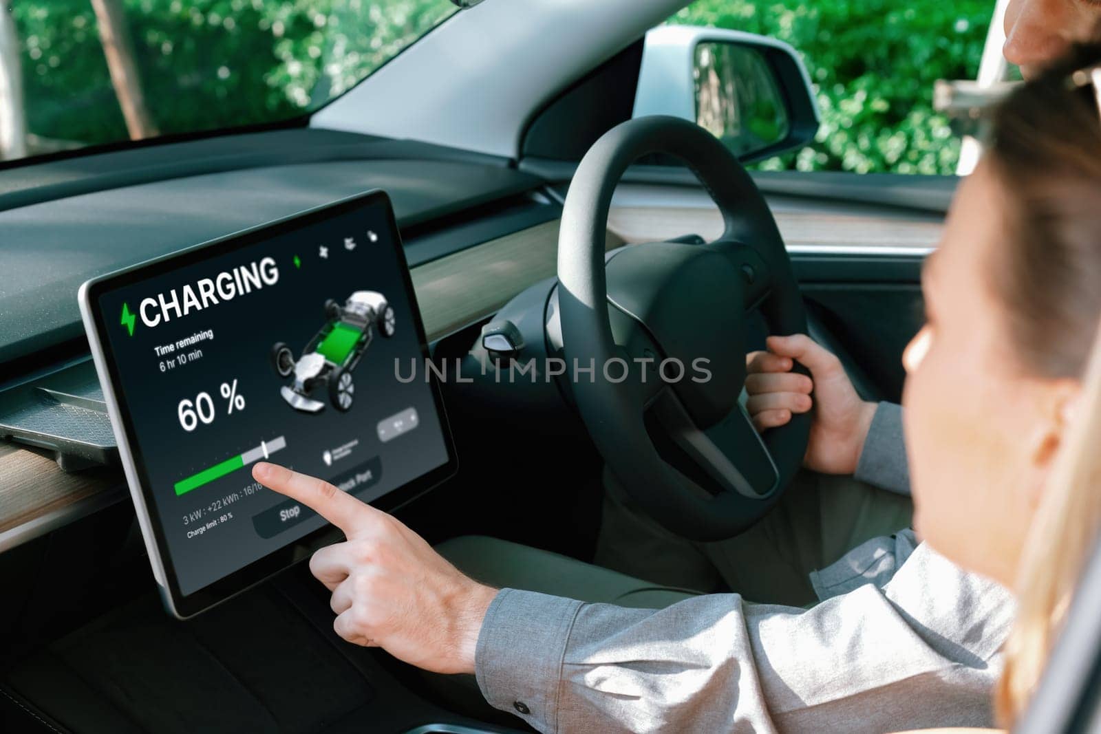 Electric car driver checks battery charging status, range and charging limit on app screen in the car. Smart technology device show EV car recharging data of electric storage in car battery innards.