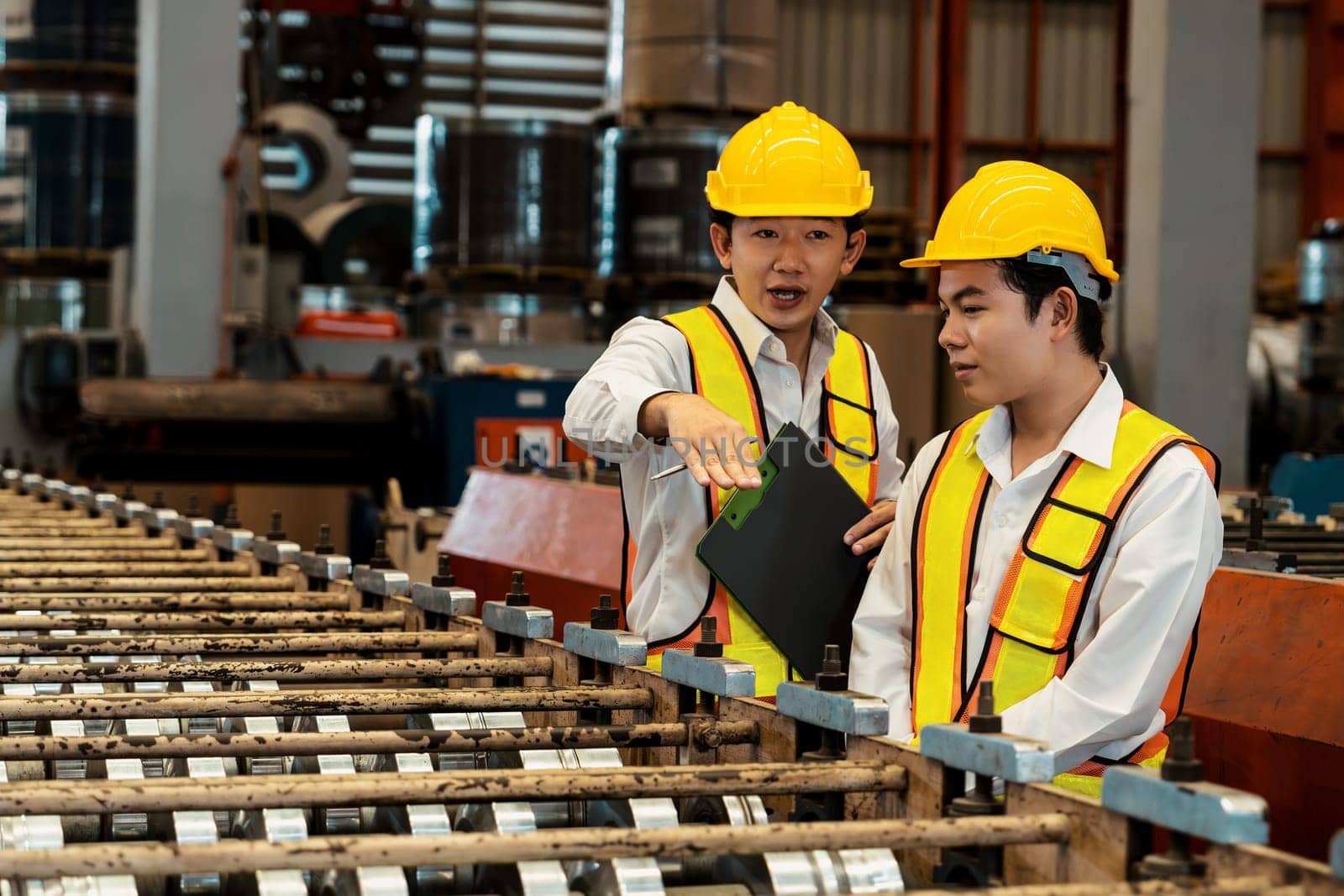 Factory worker operating metal stamping machine while supervised by engineer for optimal quality output of industrial goods on assembly steel forming line in heavy industry factory. Exemplifying