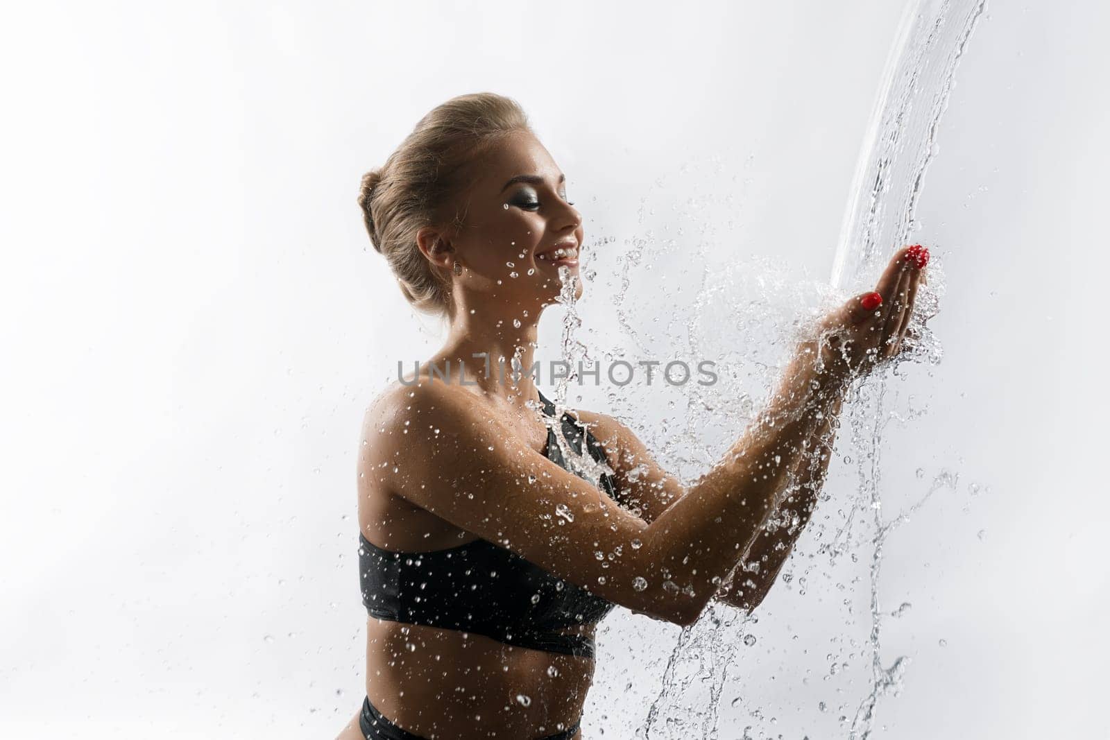 Young happy girl enjoying water stream falling in her hands from above studio shot