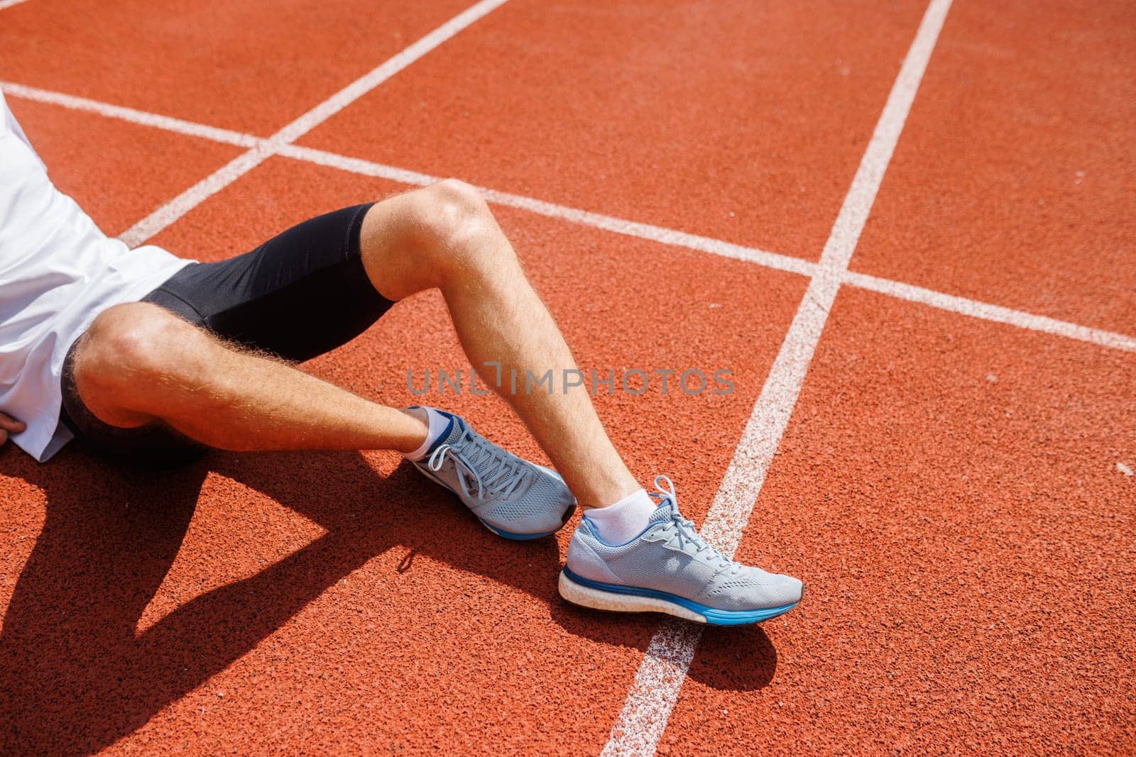 A runner resting on a track after a run, wearing athletic shoes and shorts.