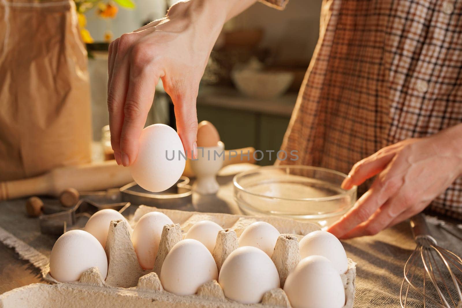 Hand taking chicken egg from box on kitchen table close-up against kitchen atmosphere