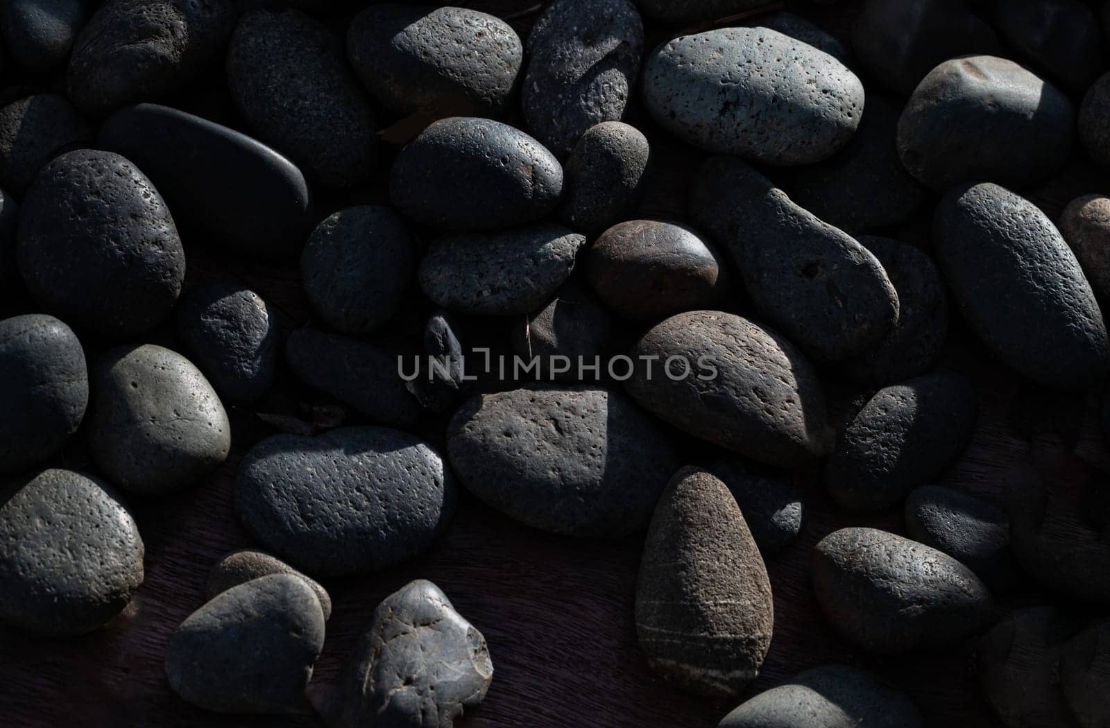 View of Light and Shadow on Black pebbles with Natural Textured Surface. Detail stone cobblestone as a background, Light and Shadow, Space for text, Selective focus.