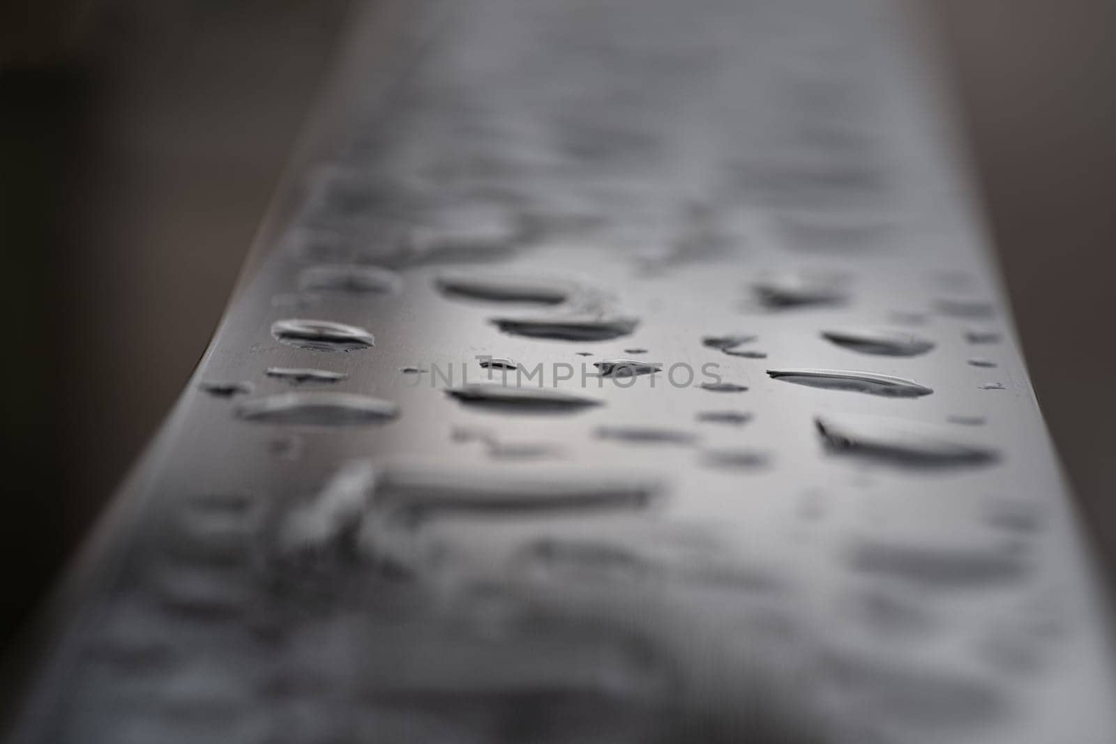 Close up of Rain water drops on the metallic surface. Water droplets caused by rain perched on a stainless steel handle, Natural Pattern of raindrops or dew drops on silver metal background for wallpaper poster and banner design, Selective focus.