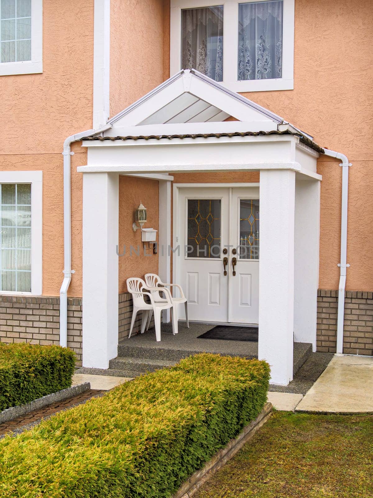 Entrance of residential house under transparent porch with two white chairs at the door.