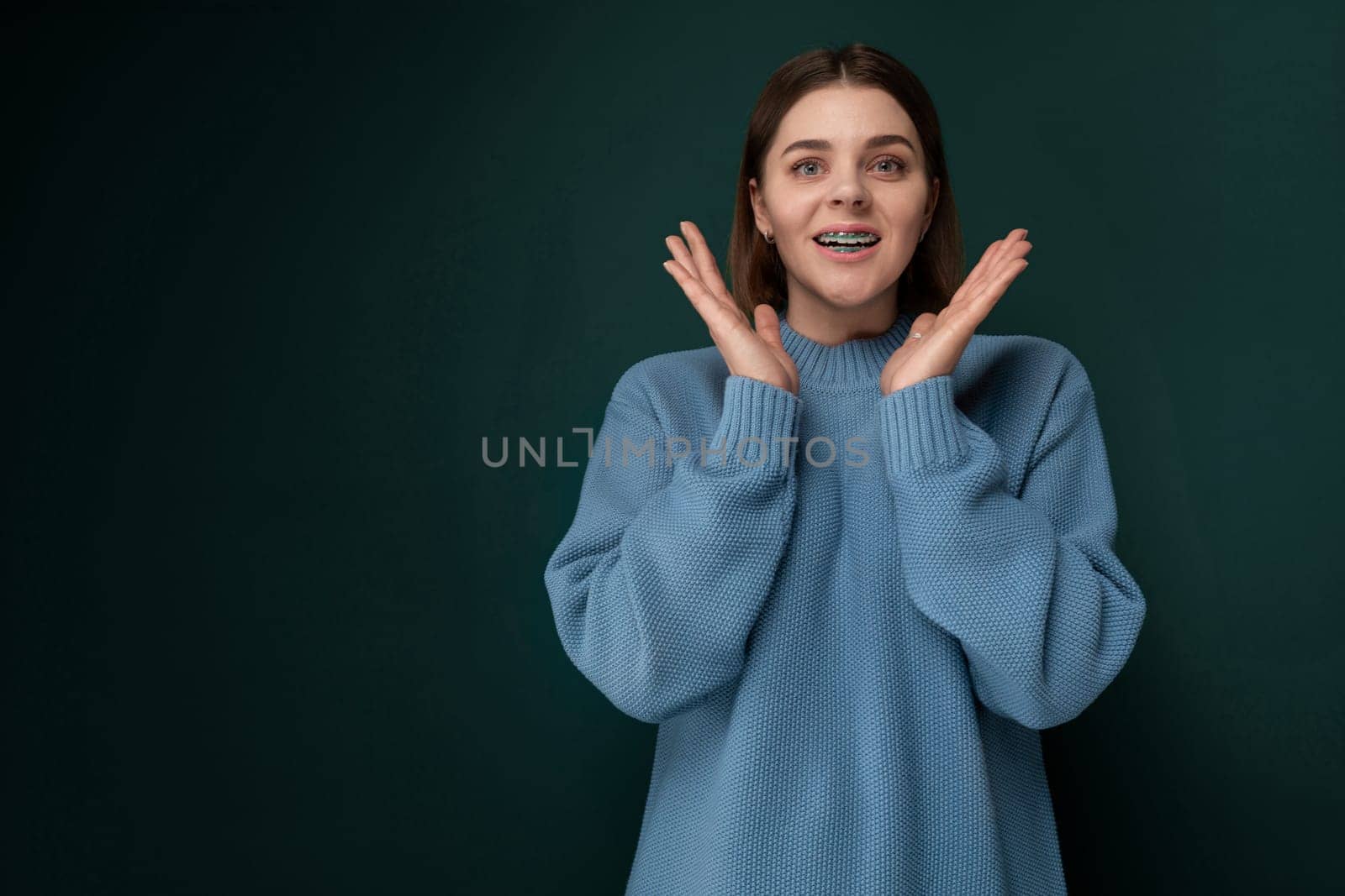 A woman wearing a blue sweater is standing with her hands raised in the air. She looks determined and confident in her posture.