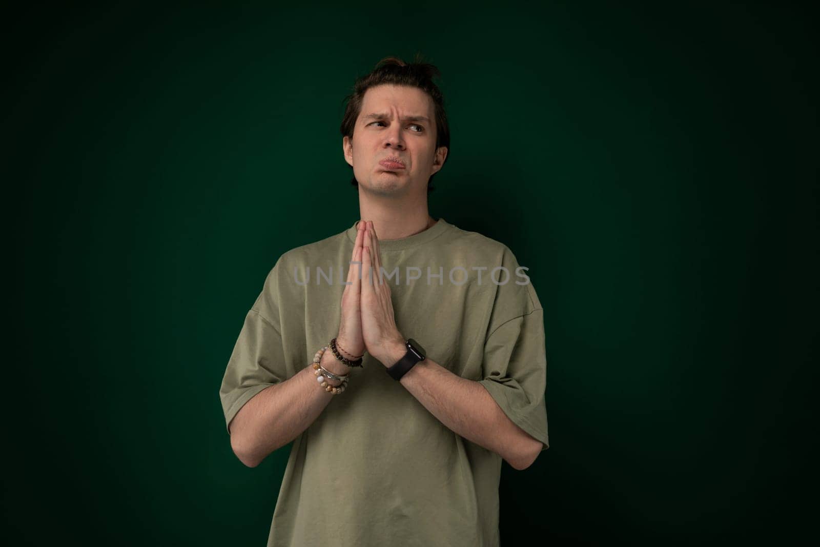 A man is standing upright in front of a vibrant green wall. The man appears relaxed and is looking straight ahead. He is wearing casual clothing and appears to be stationary.