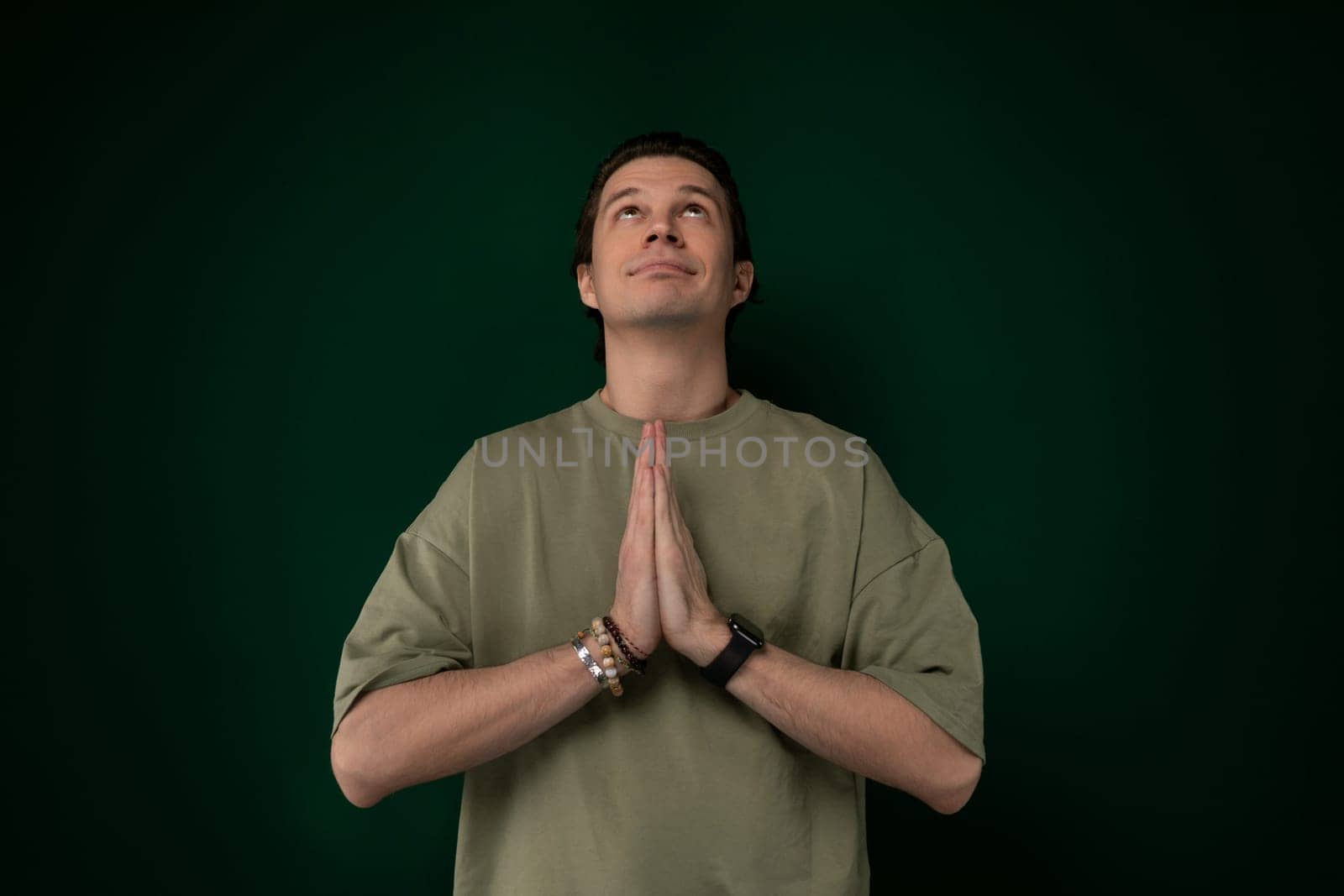 A man is standing upright in front of a solid green wall. He appears to be looking straight ahead with hands by his sides, creating a simple and straightforward composition.