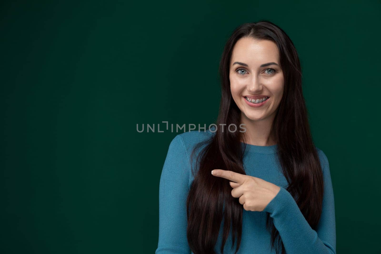 A woman is using her index finger to point at an undisclosed object or direction, drawing attention to it with her gesture. Her hand is extended, and her body language appears focused on the target at which she is pointing. The background shows a simple and neutral setting, allowing the viewer to solely focus on the womans action.