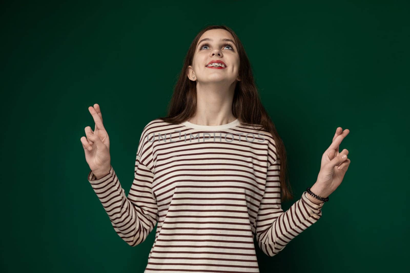 A woman is standing in front of a vibrant green wall. She appears contemplative while looking in the distance. The contrast between her figure and the wall creates a striking visual impact.
