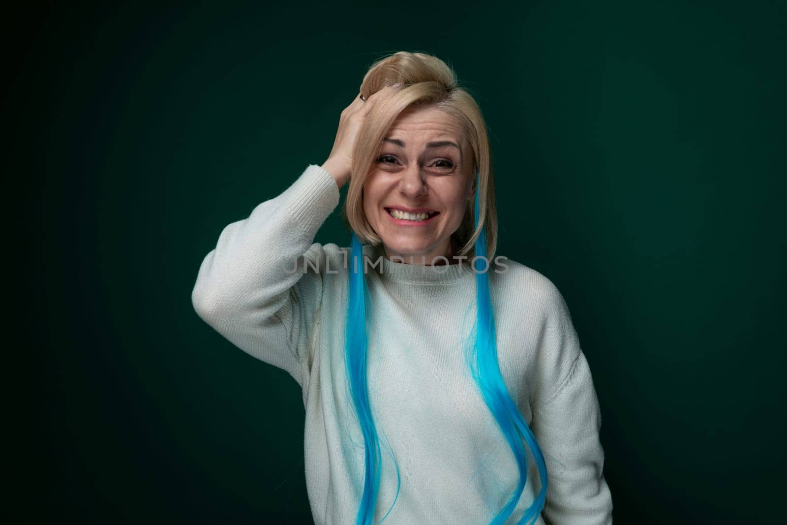 A woman with vivid blue hair is wearing a cozy white sweater, standing confidently. Her striking hair color contrasts with the neutral sweater, creating a bold and modern look.