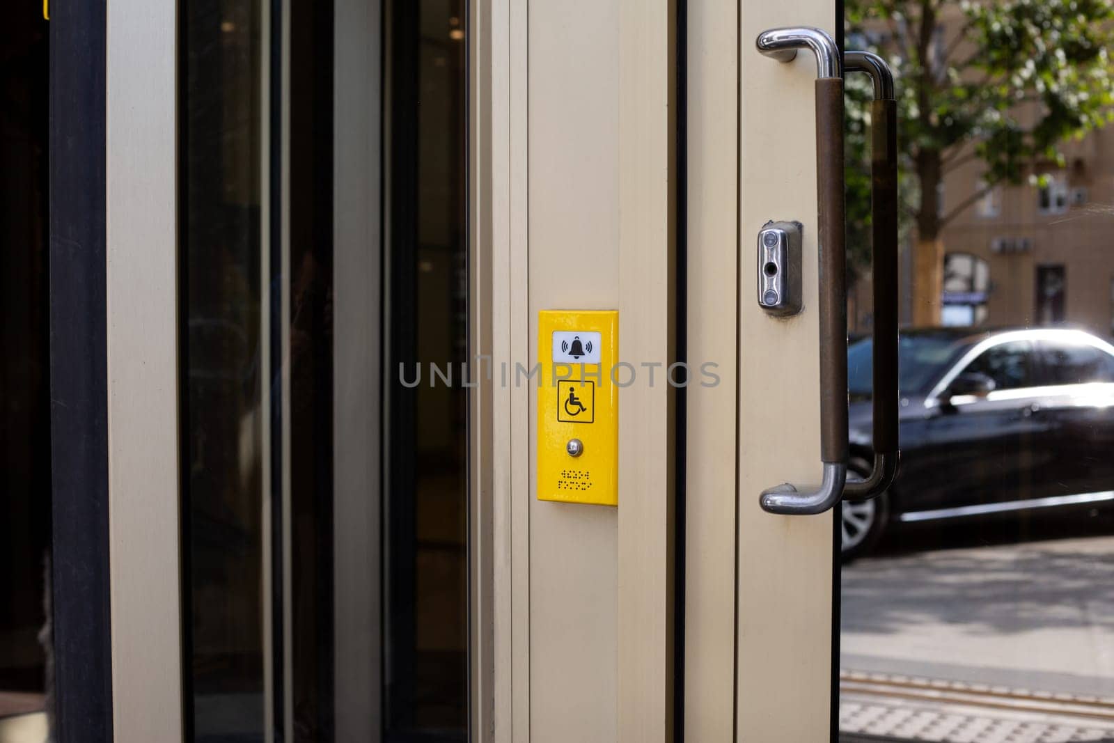 Modern panel with help button for people with disabilities near building door, sign with wheelchair sign and bell to call assistance staff for disabled people and braille text for blind person