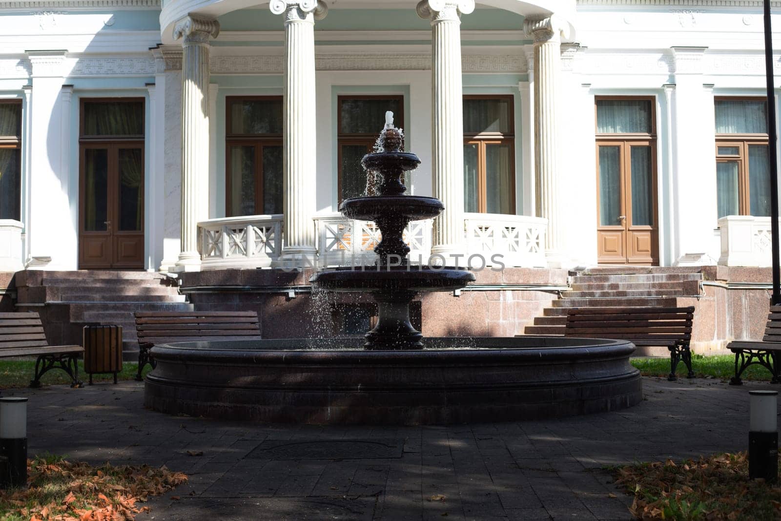 Old fountain in backyard against the background of building facade with columns in street park for people to rest. Pedestrian path near stone fountain