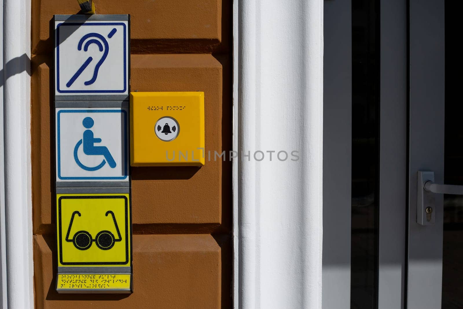 Set of signs characterizing people with disabilities next to button for call help on building wall. Disabled person symbol next to deaf and blind person symbol with braille text for finger reading
