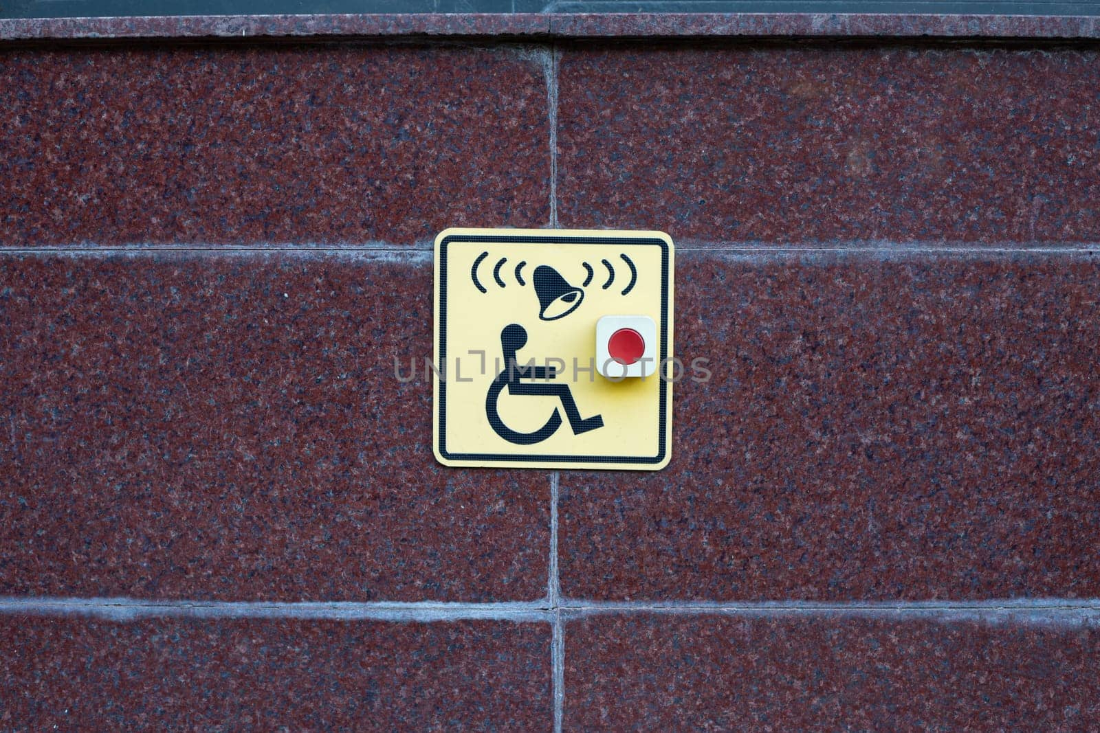 Wheelchair sign next to button to call help on street wall. Accessible area for people with disabilities, moving people in wheelchairs in modern city