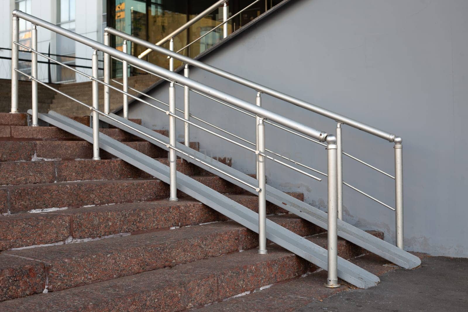Metal ramp with handrails for grip for access to building on staircase for people on wheelchair. Accessible environment for people with strollers and wheelchair for rolling up steps