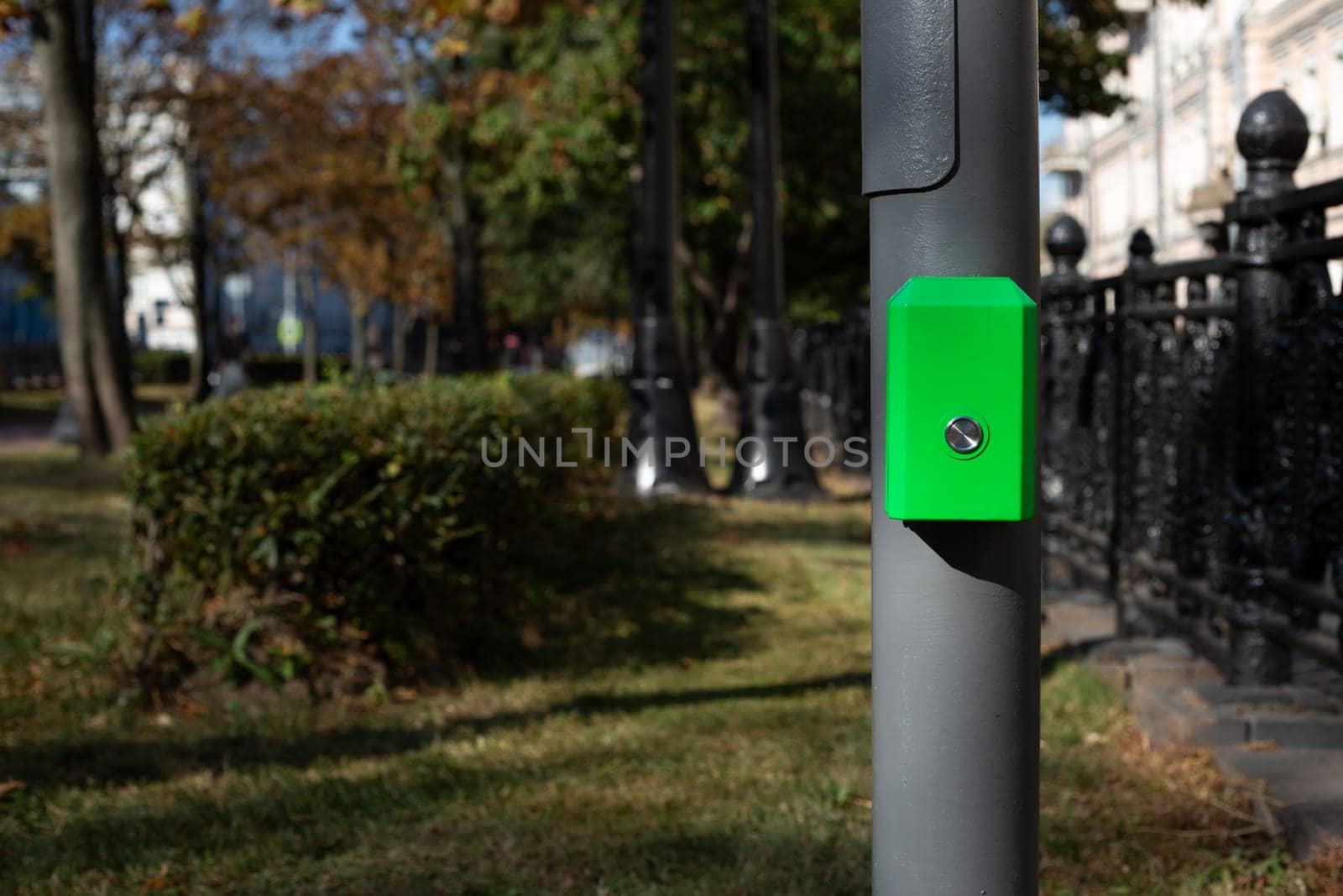 Control panel with button for pedestrians on pole, activate green traffic light signal for crossing the road along street in modern city against the backdrop of park