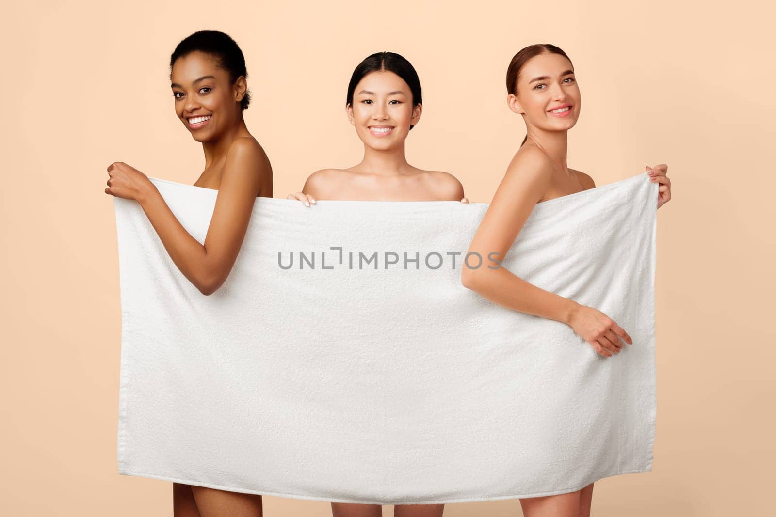 Beauty And Skincare. Three Diverse Women Posing Covering Bodies With Bath Towel Standing On White Studio Background