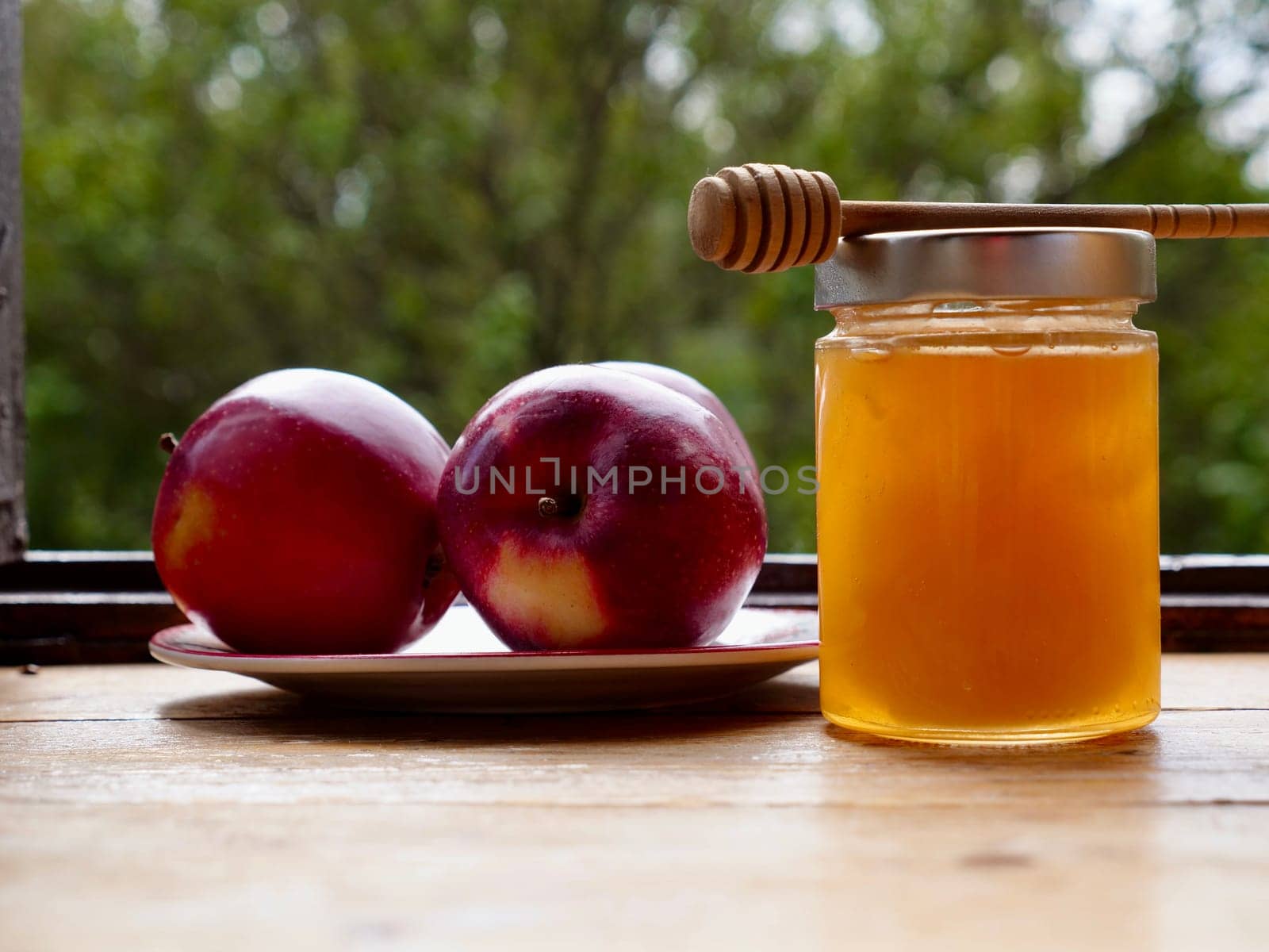 Apples red whole and sliced with a jar of honey on the traditional Jewish holiday of Rosh Hashana on a wooden table by the window on a sunny day. Close-up
