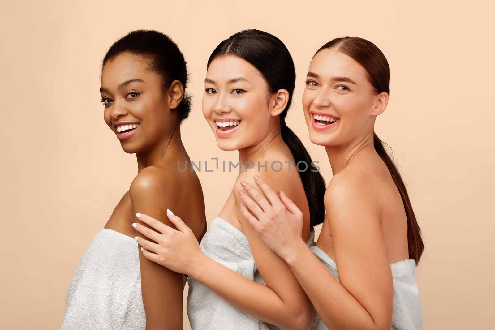 Beauty And Skincare. Three Mixed Model Girls In Bath Towels Posing Smiling To Camera Over White Studio Background