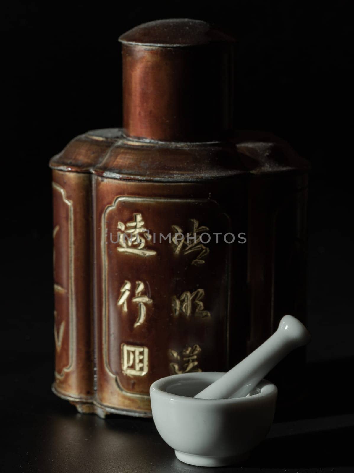Bangkok, Thailand - 18 Sep, 2024 - Small white mortar and pestle made of porcelain or ceramic (used for grinding medicinal tablets, spices) in front of Antique chinese tea leaf iron storage jar (Translation meaning chinese characther is the name of the tea). Traditional chinaese metal canister, Copy space, Selective focus.