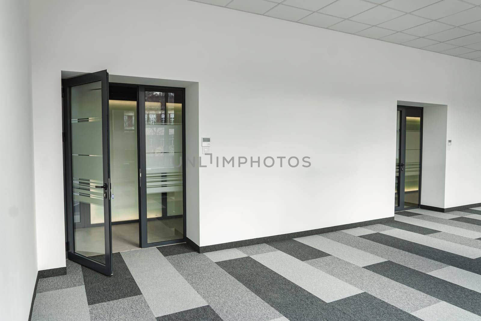 Office space devoid of furniture or decoration, containing only two doors and a black-and-white checkered floor. The doors are closed, leading to unknown destinations, while the floor adds a geometric pattern to the space.