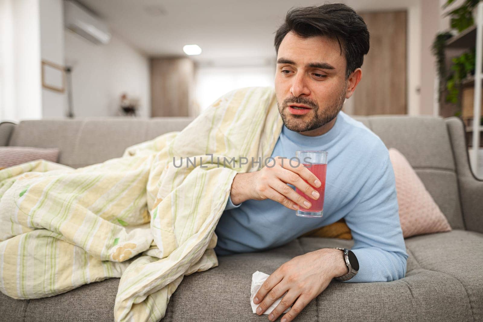 A man is seen sitting comfortably on a couch, holding a drink in his hand. He appears relaxed and content as he enjoys his beverage.