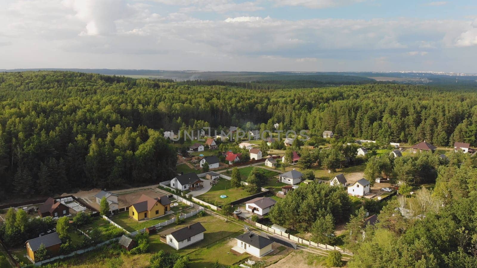 Aerial perspective of a forest surrounded residential area with new detached houses boasting green lawns and fences