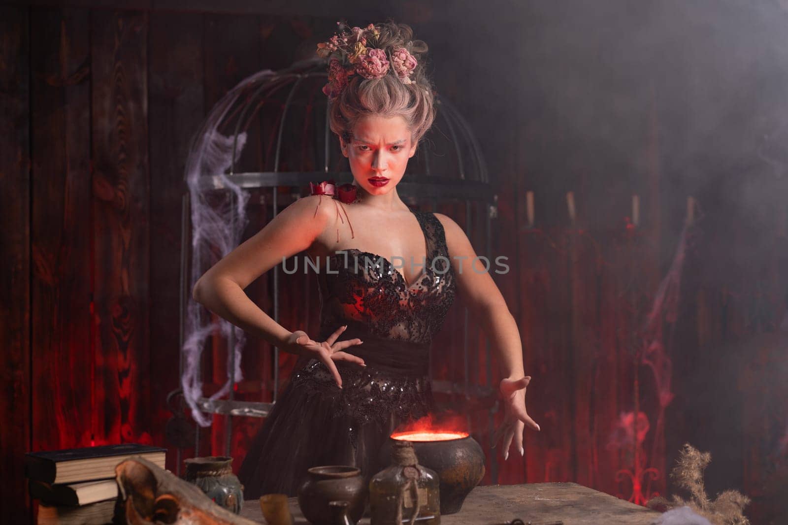 Halloween witch with cauldron. Young woman conjuring, making witchcraft standing spooky dungeon dark room. Enchantress prepare love potion using magic spell.