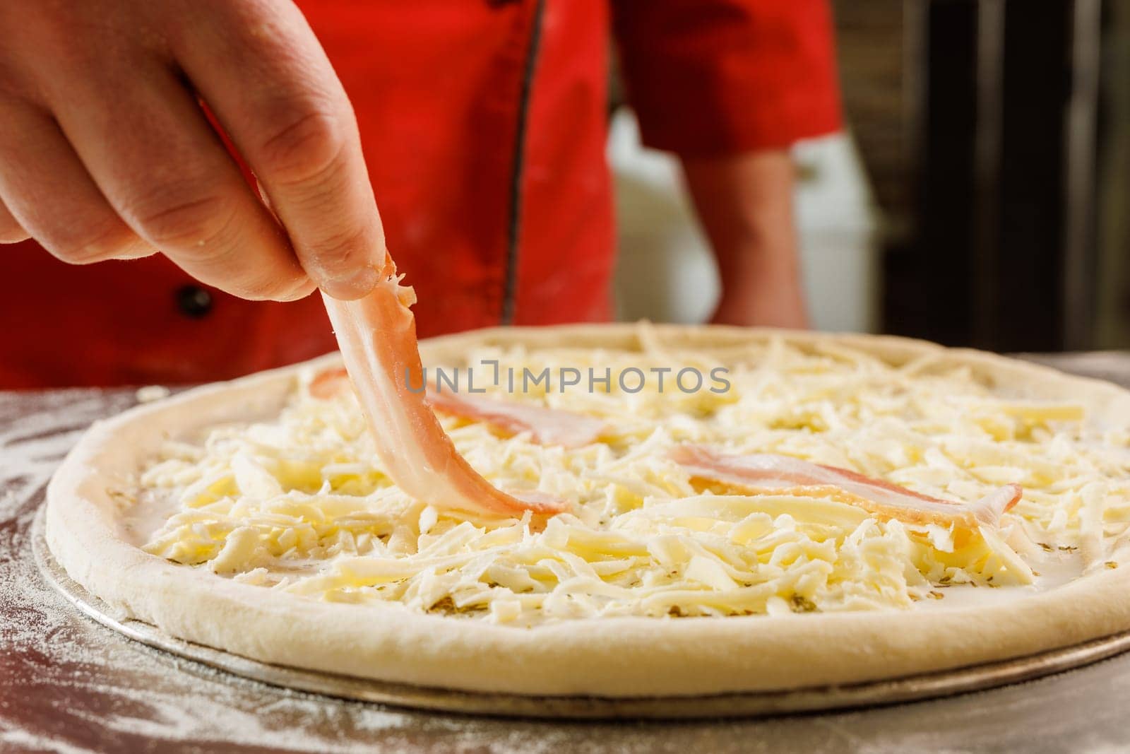 Close-up of a chef adding bacon to a cheese pizza before baking.