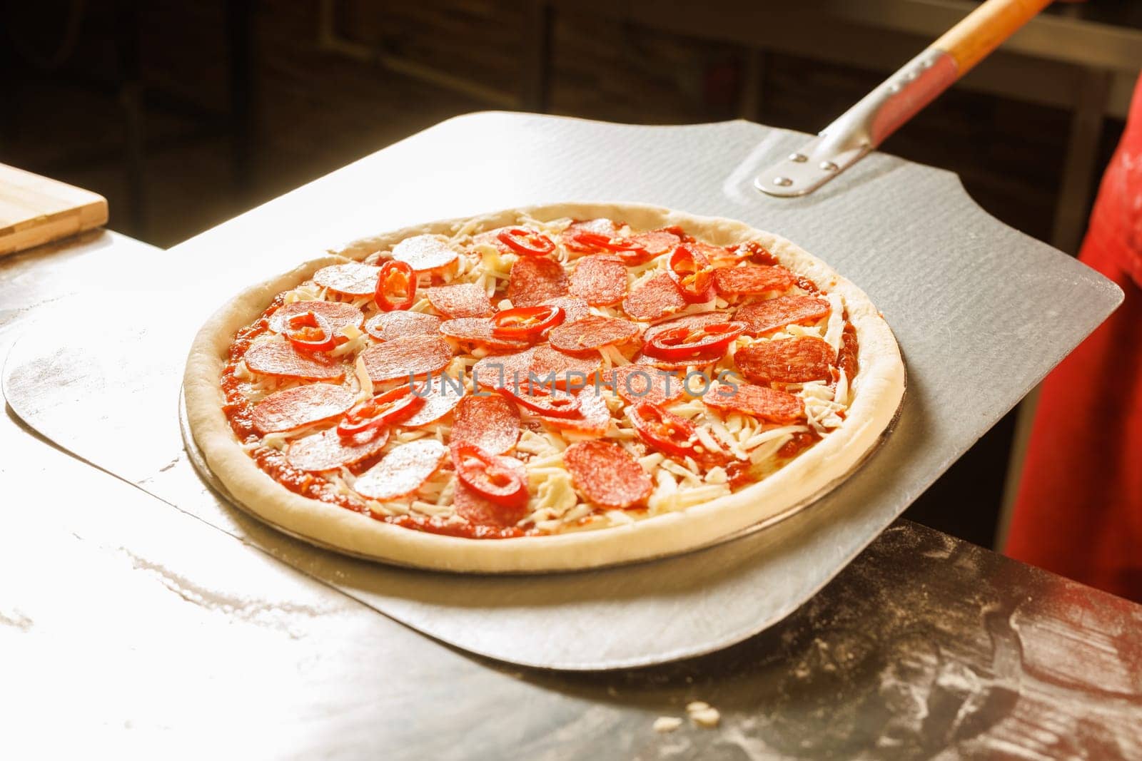 A chef in a red uniform prepares to place a pizza with cheese and tomato slices into an oven.