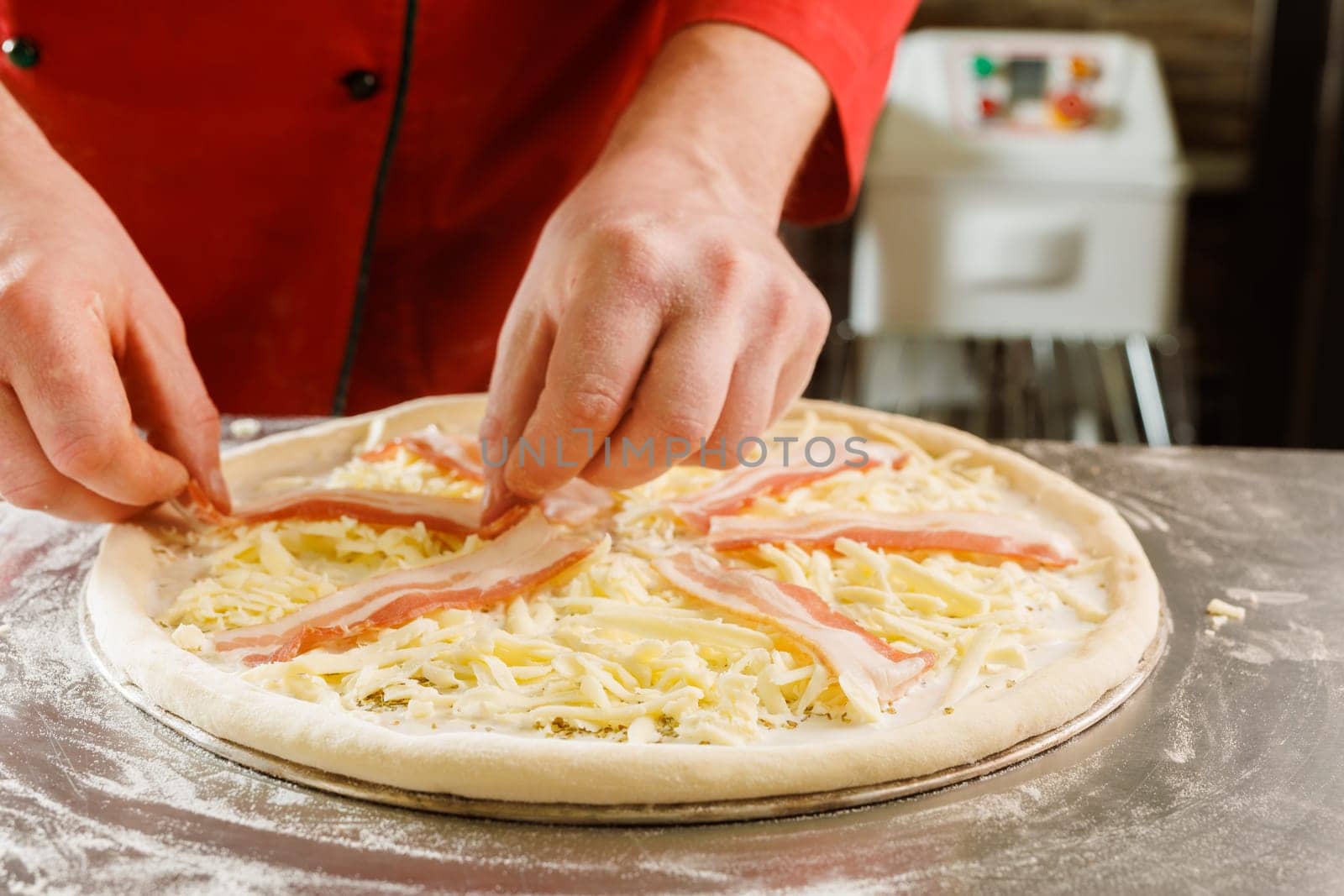 Close-up of a chef adding bacon to a cheese pizza before baking.