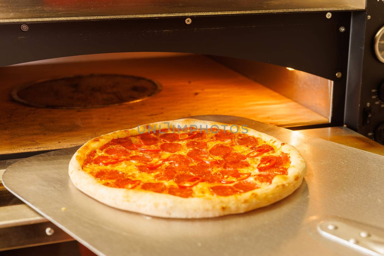 A freshly baked pizza being taken out of a pizza oven using a pizza peel.