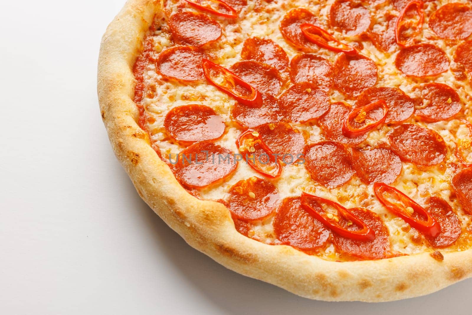 Close-up of a pepperoni pizza with red chili slices on a white background.