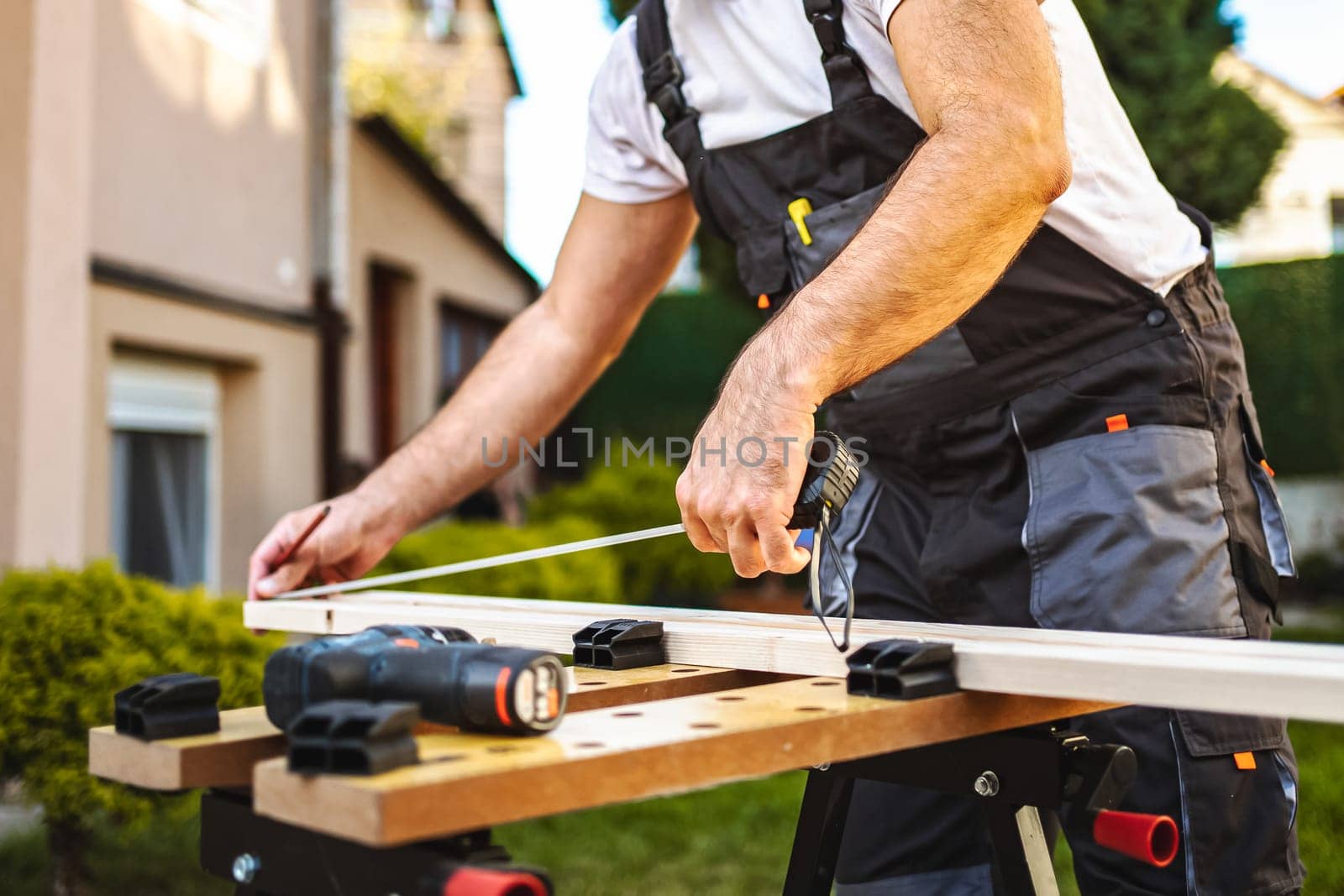 Unrecognizable male carpenter measuring wooden plank outdoors.