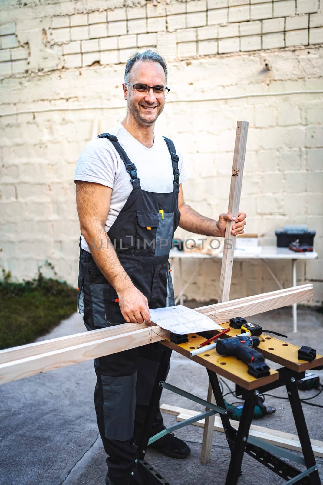 Mature male carpenter working with wooden plank outdoors.
