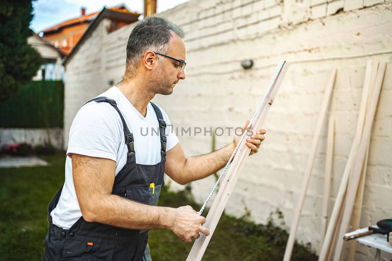 Mature male carpenter measuring wooden plank outdoors.
