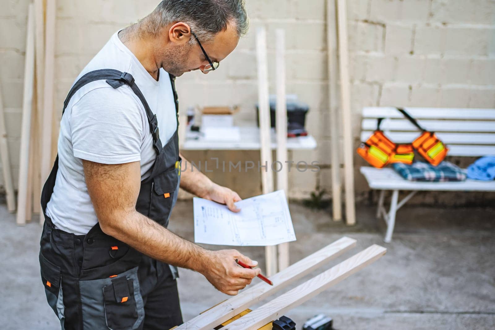 Mature male carpenter working with wooden plank outdoors.