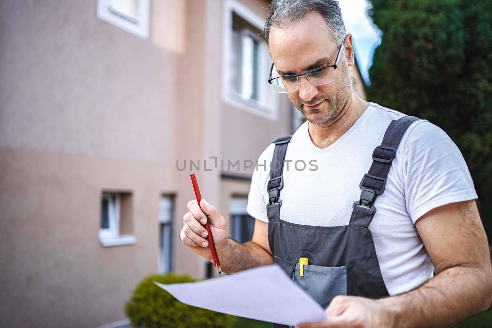 Mature male carpenter working with wooden plank outdoors.