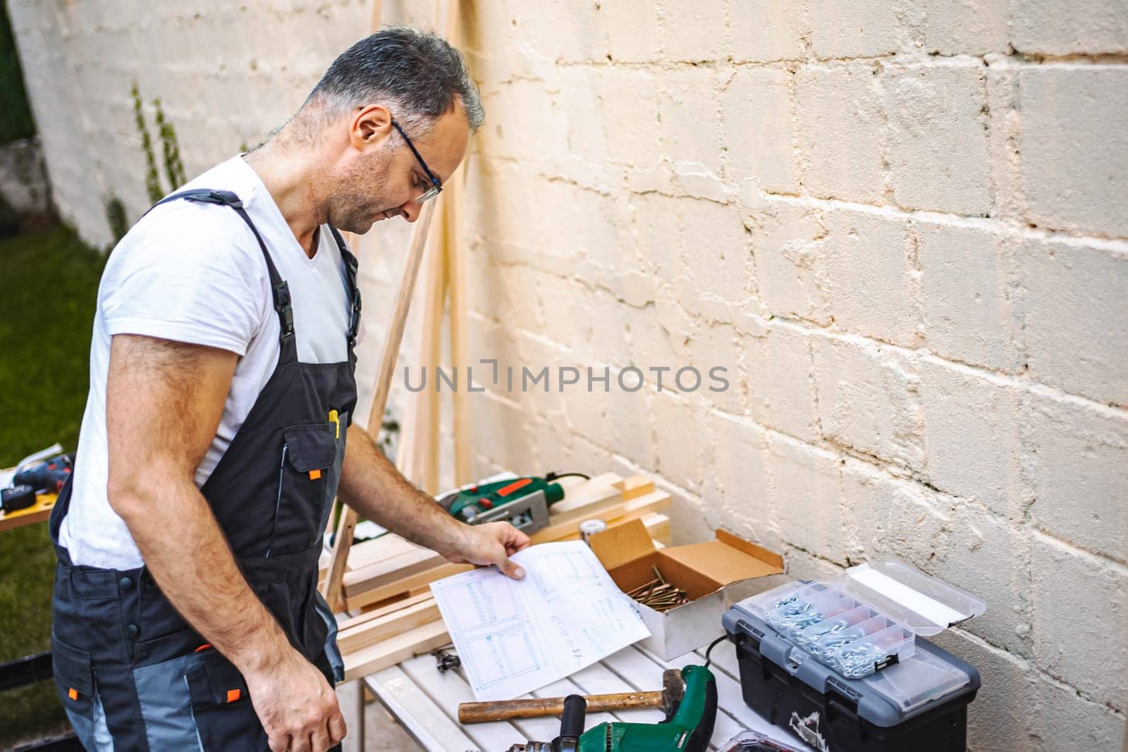 Mature male carpenter working with wooden plank outdoors.