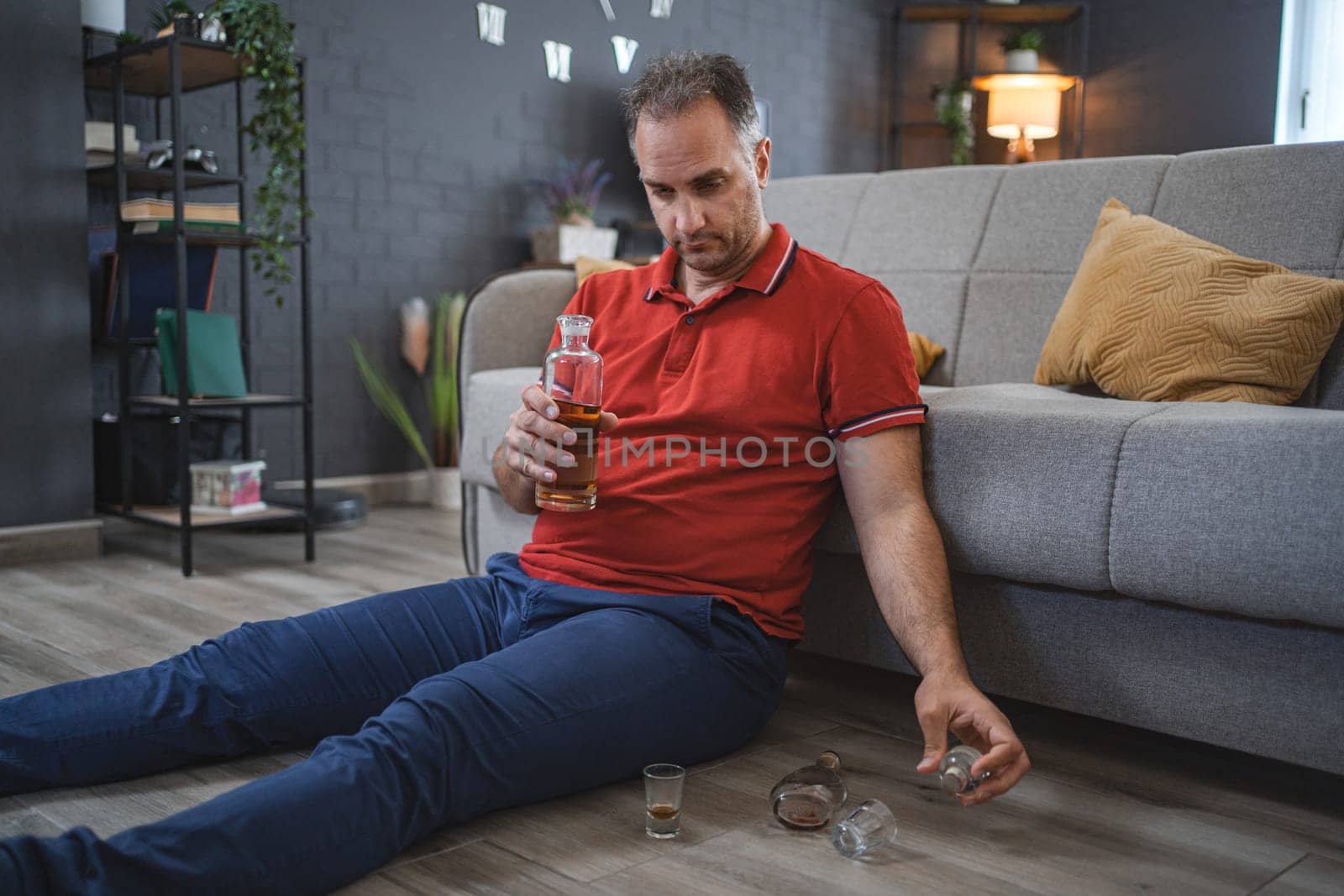 Mature man sitting on the floor and drinking alcohol.