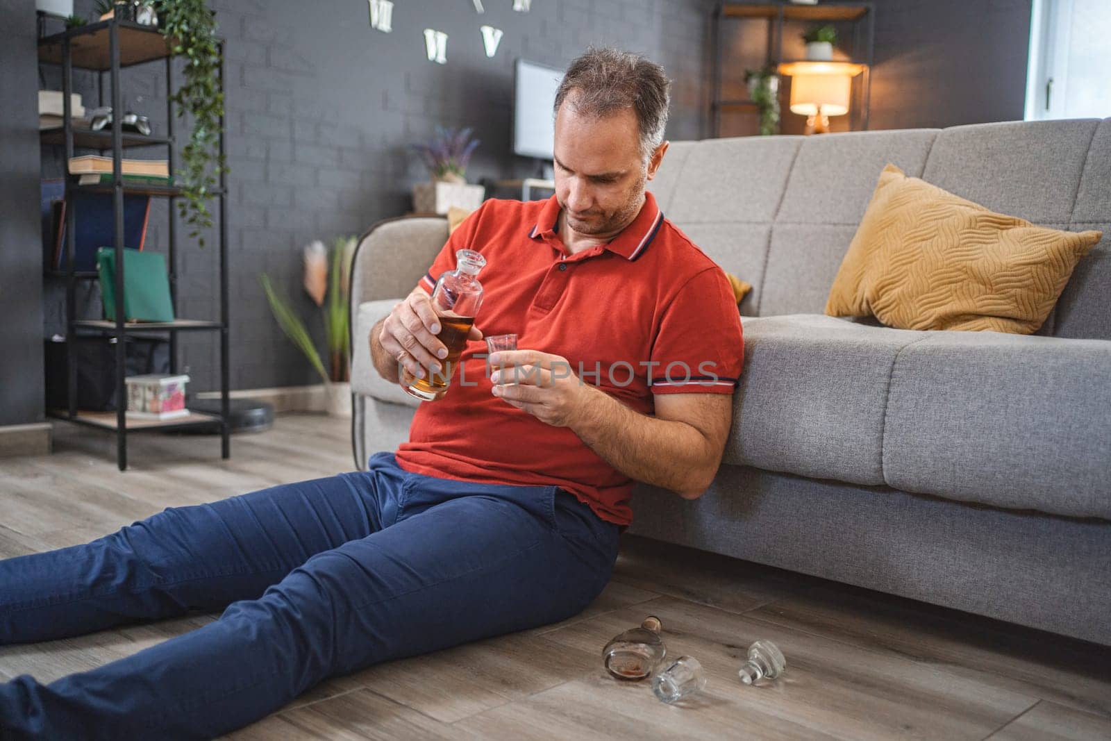 Mature man sitting on the floor and drinking alcohol.