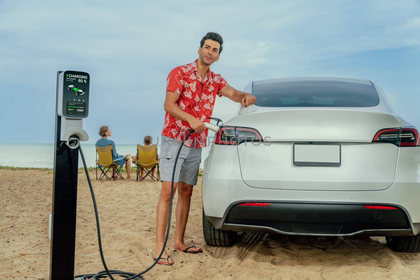 Family vacation trip traveling by the beach with electric car, dad or father recharge EV car while his family enjoy seascape beach. Family trip with alternative energy and eco-friendly car. Perpetual