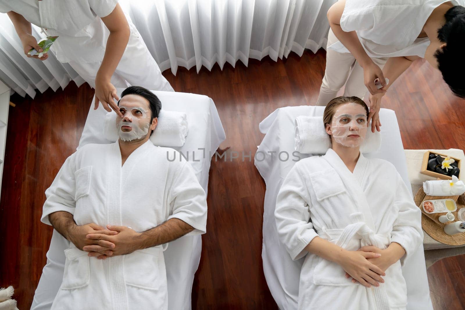 Serene modern daylight ambiance of spa salon, couple customer indulges in rejuvenating with facial skincare mask. Facial skin treatment and beauty cosmetology procedure for face. Quiescent
