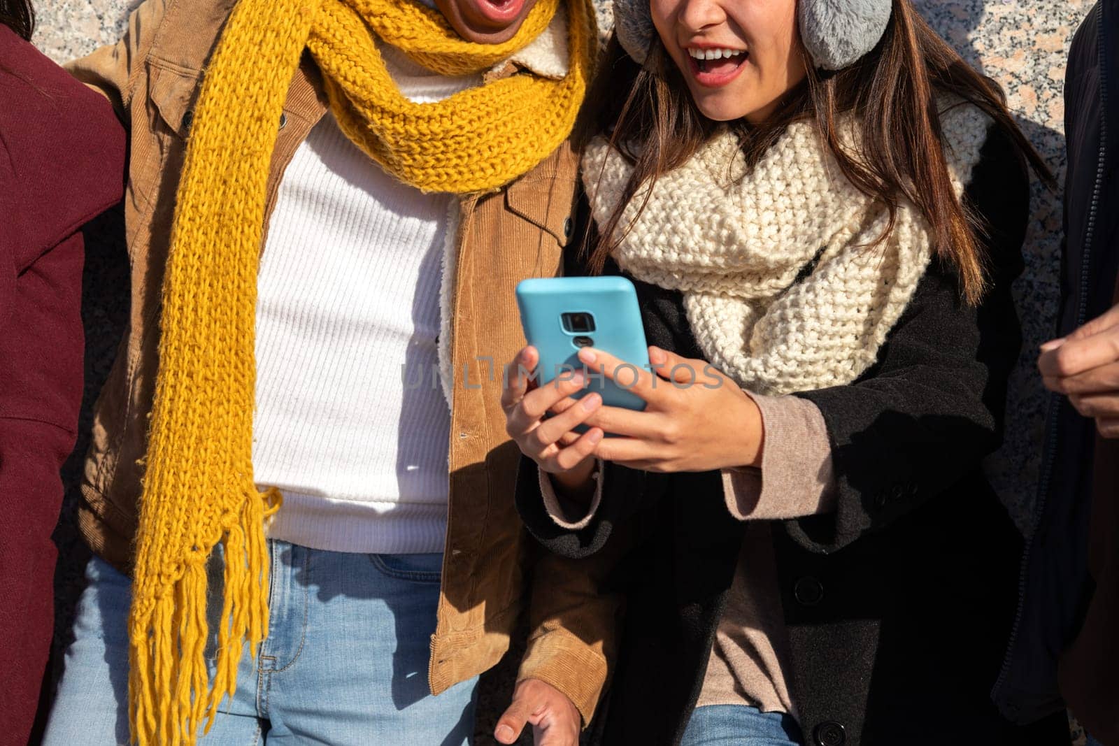 Close up of multiracial people sharing mobile phone. Students having fun using phone together during sunny winter day. by Hoverstock