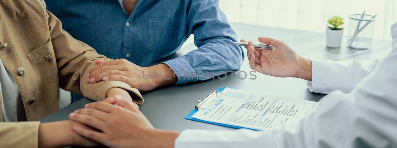 Doctor providing compassionate healthcare consultation while young couple patient holding hand, comfort each other after infertile report. Reproductive and medical fertility consulting. Neoteric