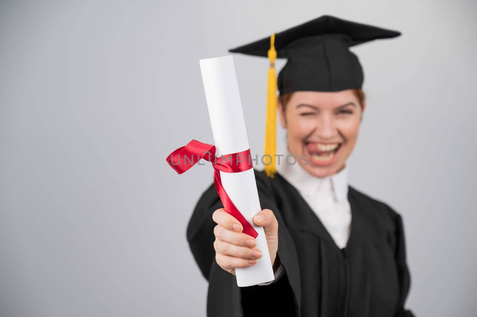 Emotional woman in graduate gown holding diploma in foreground
