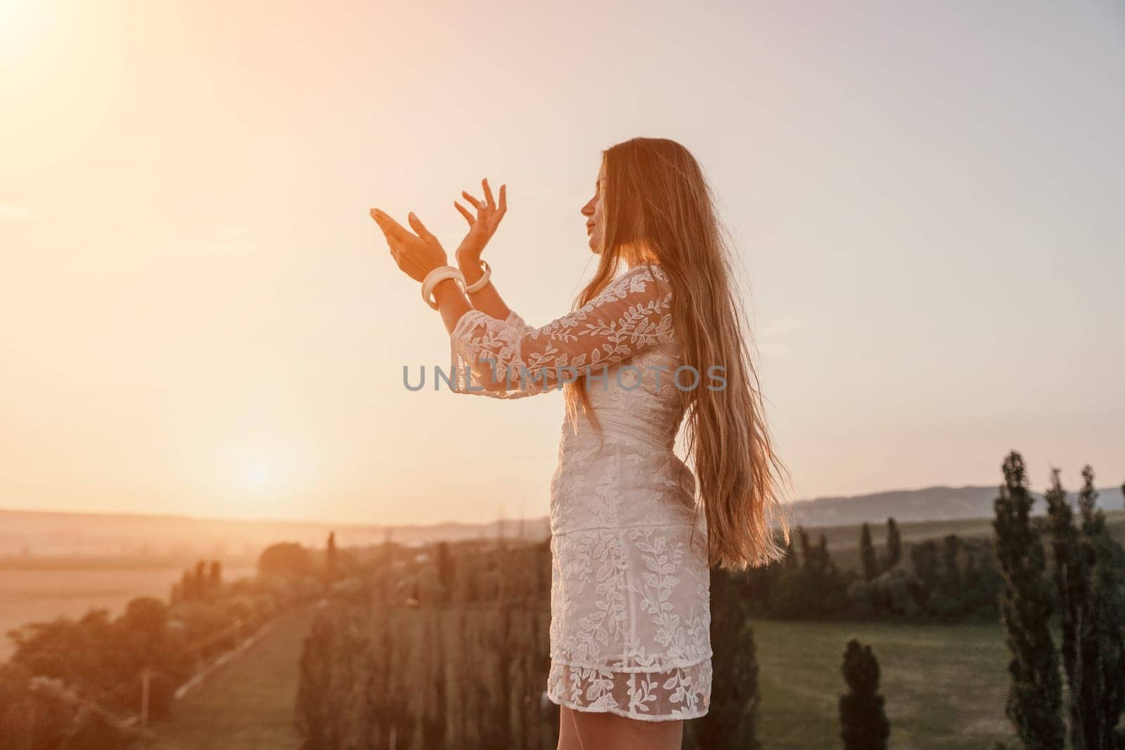 Romantic beautiful bride in white dress posing with sea and mountains in background. Stylish bride standing back on beautiful landscape of sea and mountains on sunset